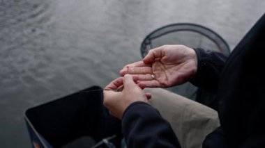 Yakından erkek balıkçının eli, balık yakalamak için oltaya yem takıyor.