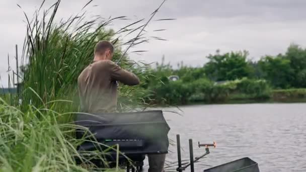 有钓竿或纺纱的渔夫和专业工具坐在河岸后视镜上 把鱼拖出湖中钓鱼 — 图库视频影像
