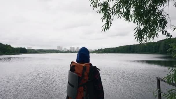 旅行者は スポーツ用品のリアビューと川と都市の背景に立っています — ストック動画