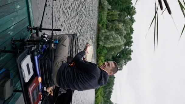 貯水池で釣りの川の岸でカープ魚を保持するプロの漁師の垂直ビデオ肖像画良いキャッチ — ストック動画