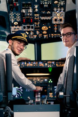 Üniformalı pilotların gülümseyen genç kaptanlarının portresi uçuş simülatörü kokpitinde uçuş hazırlığı yapıyor.