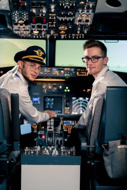 Üniformalı pilotların gülümseyen genç kaptanlarının portresi uçuş simülatörü kokpitinde uçuş hazırlığı yapıyor.