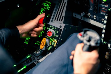 Bir askeri uçağın kokpitine yakın çekim direksiyonlu bir pilot ve uçuş simülatörünün kontrol panelinde bir sürü düğme.