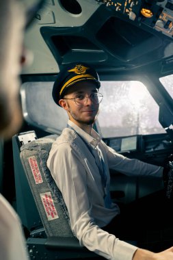 Uçağın kokpitindeki genç pilotlar uçuş sırasında hava taşımacılığını kontrol ederler. Uzak mesafe simülatörünün penceresinden güneş parlar.