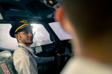 Uçağın kokpitindeki genç pilotlar uçuş sırasında hava taşımacılığını kontrol ederler. Uzak mesafe simülatörünün penceresinden güneş parlar.