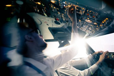 Uçağın kokpitindeki genç pilotlar uçuş sırasında hava taşımacılığını kontrol ederler. Uzak mesafe simülatörünün penceresinden güneş parlar.