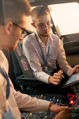 Pilotlar kontrol panelinin yanındaki kokpitte ellerinde tabletle uçuş simülatörü başlamadan önce rotayı tartışıyorlar.