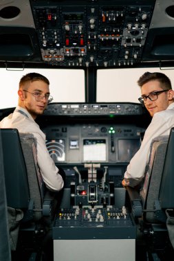 Uçuş simülatörü başlamadan önce kontrol panelinin yanındaki kokpitteki genç pilotların portreleri.