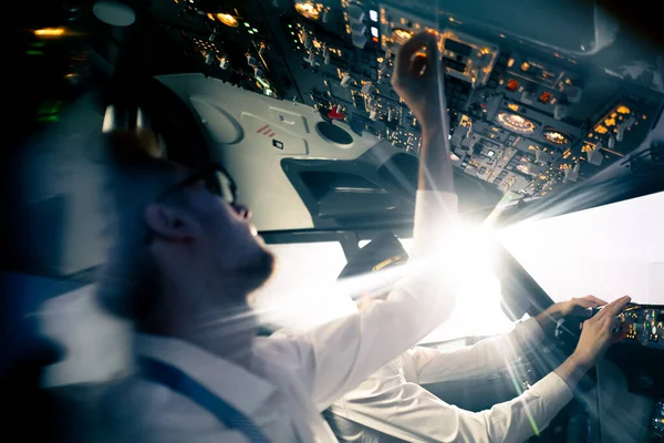 young pilots in the cockpit of the plane control the air transport during the flight the sun shines from window in the far distance simulator