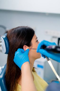 Bir KBB doktoru klinikte bir hastanın kulağına endoskopi uygular ve elinde profesyonel bir cihaz tutar.