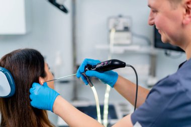 Bir KBB doktoru klinikte bir hastanın kulağına endoskopi uygular ve elinde profesyonel bir cihaz tutar.