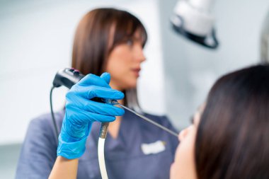 KBB doktoru, klinikte elinde profesyonel bir aletle hastanın burnunun endoskopisini yapar.