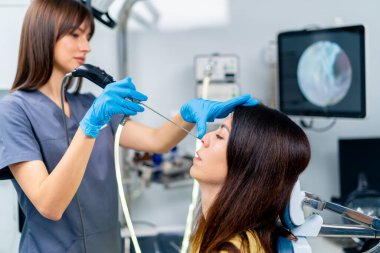 KBB doktoru, klinikte elinde profesyonel bir aletle hastanın burnunun endoskopisini yapar.