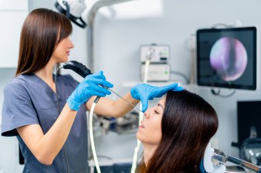 KBB doktoru, klinikte elinde profesyonel bir aletle hastanın burnunun endoskopisini yapar.