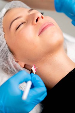 Ellerinde fırça tutan ve güzellik salonundaki kadın bir müşterinin yüzüne ve boynuna sağlık maskesi takan eldivenli güzellik uzmanının elleri.