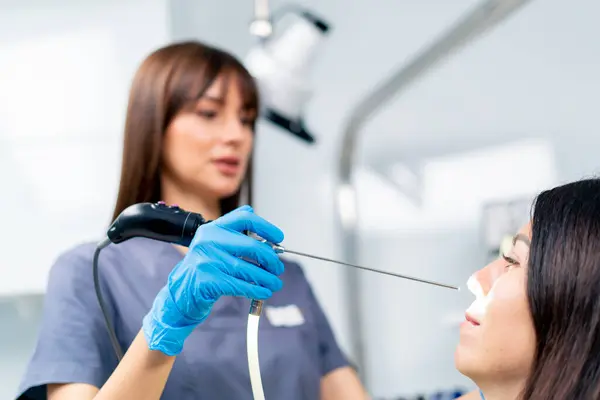 KBB doktoru, klinikte elinde profesyonel bir aletle hastanın burnunun endoskopisini yapar.