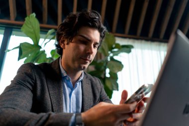 Ofiste dizüstü bilgisayarla çalışan ciddi bir iş adamının portresi akıllı telefonla borsanın düşüşünü kontrol ediyor.