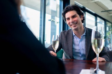 Bir restoranda bir kızla oturmuş bir bardak şampanyayla gülümseyen yakışıklı bir adamın portresi.