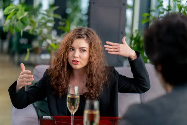 同僚とのビジネスミーティングやメガネのシャンパンを持つ男性とのデートで口論する若い動揺したカーリー女性の肖像画 — ストック写真