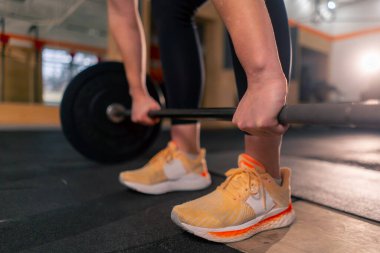 Spor salonunda siyah taytlı bir kız antrenör ağırlığıyla halteri kaldıracak.