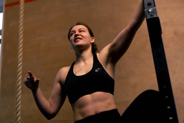 Spor salonunda siyah taytlı bir koç ve üstü açık bir kız yatay bara tırmanıyor.
