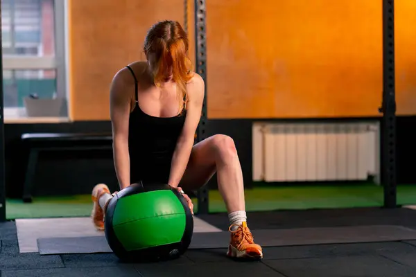 在一家体育俱乐部里 红头发的教练靠在球上为她的腿做热身运动 — 图库照片