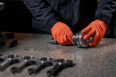 Masadaki bir benzin istasyonunda genç bir motor tamircisi yeni bir piston parçası monte ediyor.