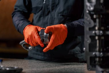 Masadaki bir benzin istasyonunda genç bir motor tamircisi yeni bir piston parçası monte ediyor.