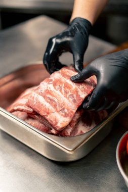 Profesyonel mutfak elemanlarına yakın plan siyah eldivenli kaburgaları bir kaseden alıp bir tahtaya transfer edin.