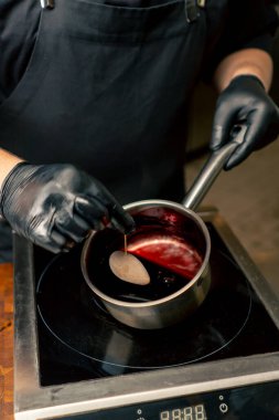 Profesyonel bir mutfak aşçısına yakın siyah eldivenli bir aşçı tavadan çıkan bordo sosuyla lezzeti emer.