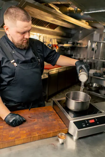 Professional Kitchen Chef Black Jacket Sizzles Salt Saucepan Standing Stove — Stock Photo, Image