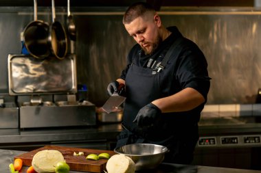 Profesyonel mutfakta siyah eldivenler giyerek yeşil bir elmayı kesip bir kaseye boşaltıyor.