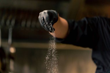 Profesyonel bir mutfakta, siyah eldivenlerle demir bir kasede lahana tuzlarken.