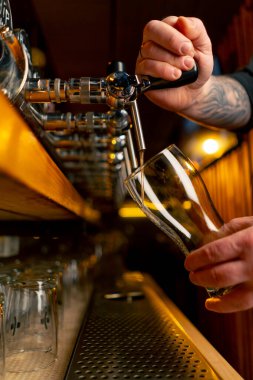 Bar tezgahındaki birahanede yakın plan barmenlerin elleri bardağa hafif bira döker.