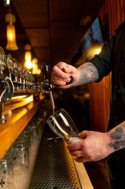 Bar tezgahındaki birahanede yakın plan barmenlerin elleri bardağa hafif bira döker.