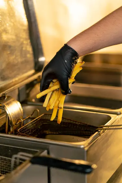 穿着黑色手套的专业厨房厨师的特写镜头把薯条放进了一个很深的炸薯条里 — 图库照片