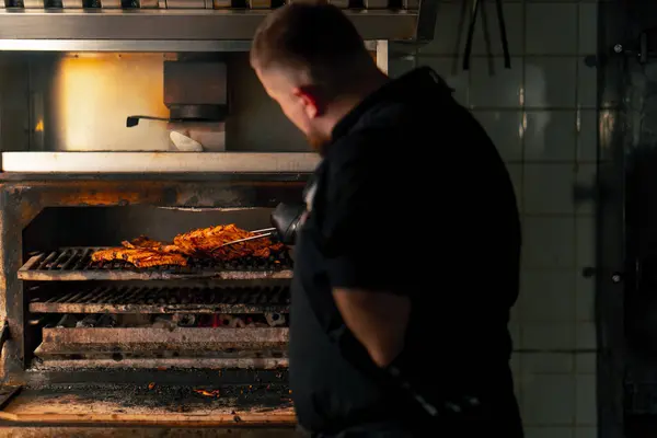 在热烤箱旁边穿着黑色夹克的专业厨房厨师翻开排骨 — 图库照片