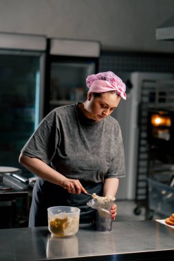 Profesyonel bir mutfakta kadın fırıncı krema macununu pasta poşetine aktarıyor.
