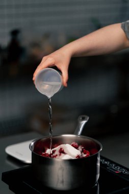 Profesyonel mutfağa yakın plan. Kirazlı tencereye su dök.