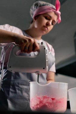 Profesyonel bir mutfakta, krem ve boyayı mikserle karıştıran bir kadın fırıncının düşük pozu.