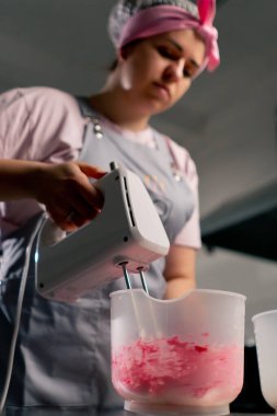 Profesyonel bir mutfakta, krem ve boyayı mikserle karıştıran bir kadın fırıncının düşük pozu.