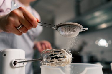 Profesyonel bir mutfak serpintisi içinde kadın bir fırıncının elek içinde pudra şekeri ile yakın plan fotoğrafı.