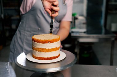Profesyonel bir mutfakta kadın fırıncıyı kapatıyordu. Süngerli kekin üzerine krema dağıtıyordu.