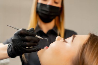 Bir dişçi, bir kızın diş muayenehanesinde bir kızın ağız boşluğunu muayene eder.