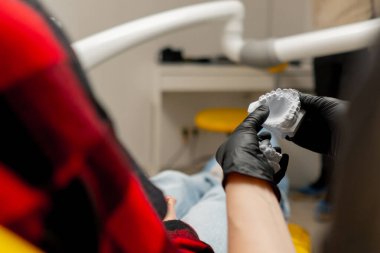 Kapalı gişe dişçi esmer dişçi siyah üniformalı dişçi diş kalıbı gösteren bir kıza danışıyor.