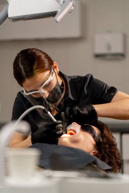 Diş hekimi kız dişçi, beyazlatma işleminden önce genç bir adama temizlik yapıyor.