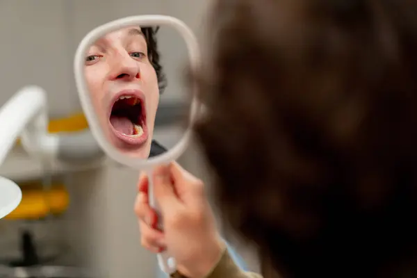 Diş muayenehanesini kapatın. Genç bir adam sandalyeye oturur ve diş aynasından dişlerine bakar.