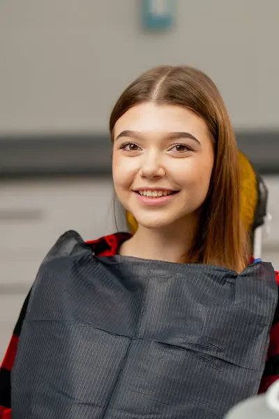 Ofisteki bir dişçi kız hastaya yakın çekim. Sandalyeye oturmuş, mutlu ve sırıtan bir pislikten korunuyor.