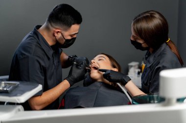 Diş muayenehanesinde asistanı olan bir erkek dişçi genç ve güzel bir kıza anestezi iğnesi yapar.