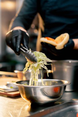 Siyah eldivenli şefi kapat. Farklı malzemeleri maşayla topuz yap.